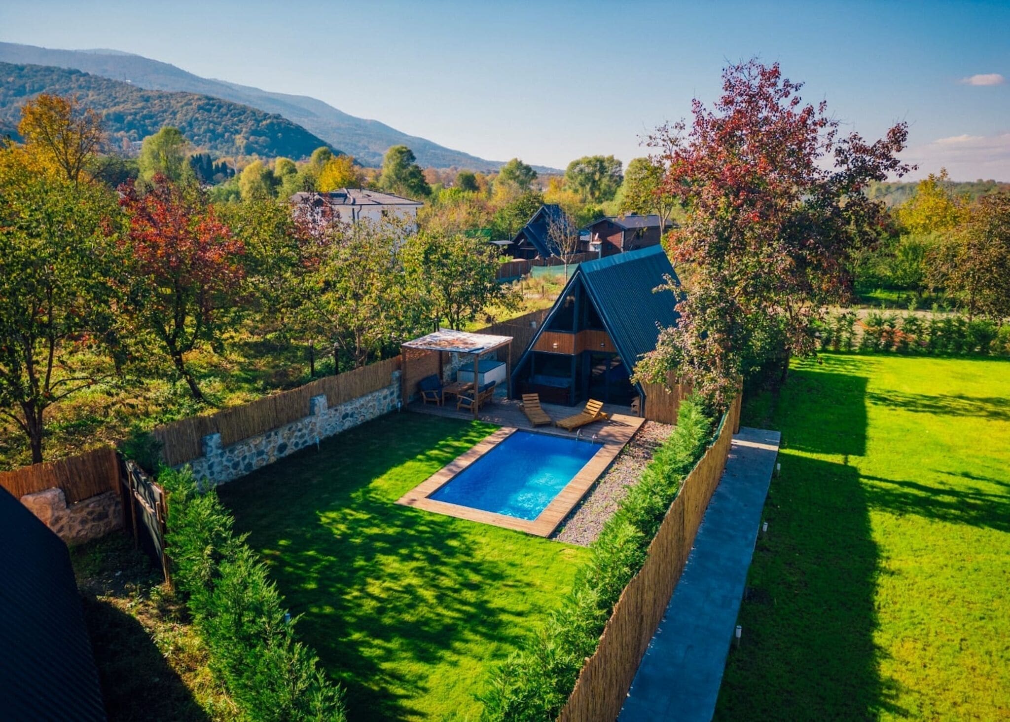 Una casa moderna con piscina, rodeada por un jardín cuidado y vistas a las colinas.