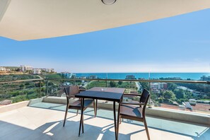 Een balkon met een tafel en stoelen, met uitzicht op de zee en omliggende gebouwen.