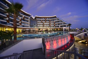 Een modern hotel met een groot zwembad, meerdere balkons en een goed verlicht buitengebied.
