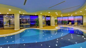 Una piscina interior con diseño curvo, paredes de vidrio y zonas de estar.
