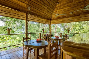 An outdoor wooden deck with tables and chairs, surrounded by lush greenery. - Drake Bay Getaway Resort By Sandglass (Drake Bay)