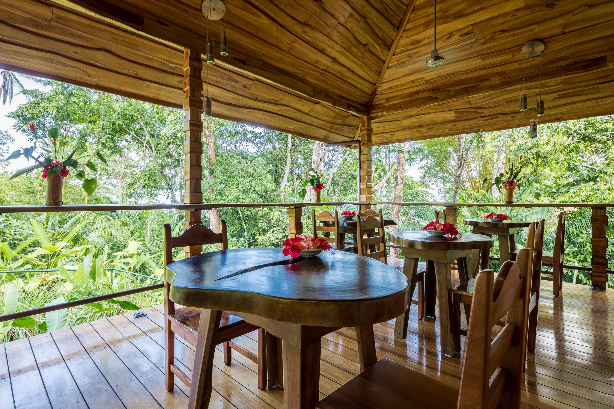 A wooden deck with tables and chairs, surrounded by lush greenery.