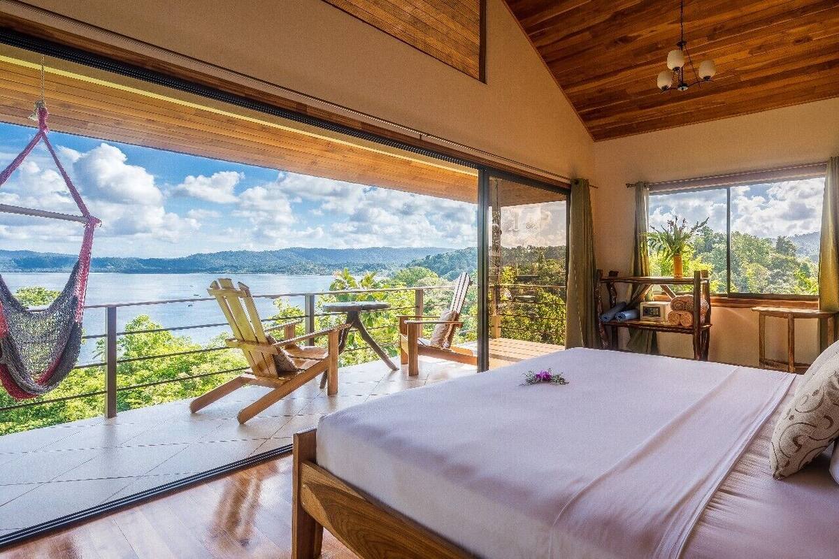 Une chambre avec un grand lit, une vue sur un lac, des meubles en bois et un hamac.