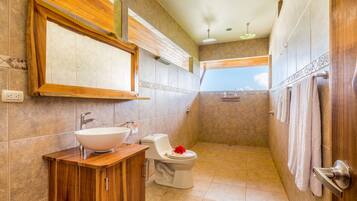 Un baño con tocador de madera, un lavabo blanco, un inodoro y zona de ducha.