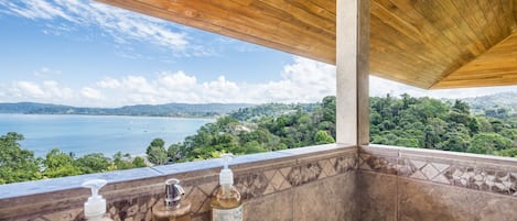 Un balcón con vistas a un lago y un bosque, techo de madera y dos botellas de líquido.