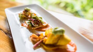 A white rectangular plate with three appetizers, each with a slice of bread topped with avocado, red onion, and a sauce.