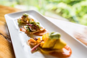 A white rectangular plate with three appetizers, each with a slice of bread topped with avocado, red onion, and a sauce. - Drake Bay Getaway Resort By Sandglass (Drake Bay)