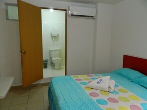 A bedroom with a bed, a red headboard, a bathroom with a toilet and shower, and an air conditioning unit. - Casa Laurel (Cancun)