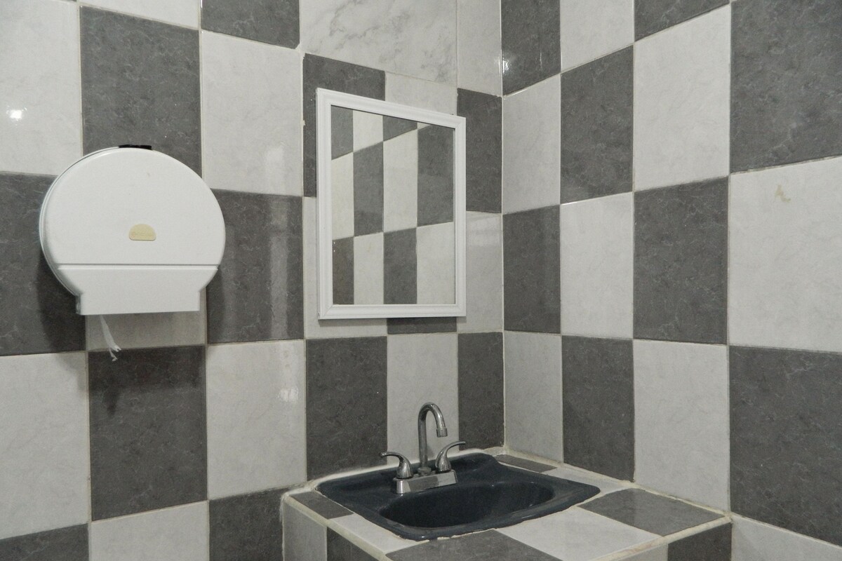 A bathroom with a checkered tile wall, a white toilet, a sink with a faucet, and a mirror.