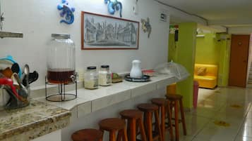 A bar area with stools, a counter with jars, a framed picture, and a yellow couch in the background.