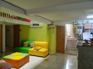 A living room with a green and yellow sofa, a small orange ottoman, a glass coffee table, and a staircase leading to another area. - Casa Laurel (Cancun)