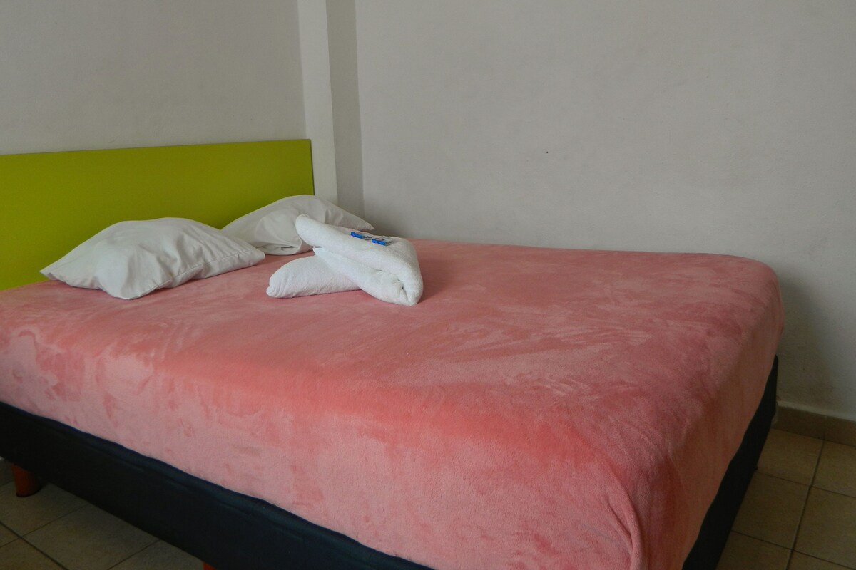 A bed with a pink bedspread, two white pillows, and a folded white towel.