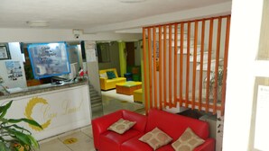 A reception area with a red sofa, a counter with a sign reading 'Casa Laurel,' and a blue television. - Casa Laurel (Cancun)