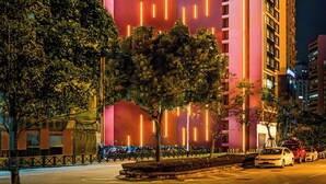 Un hotel alto con líneas verticales iluminadas en su fachada, un letrero que indica que es el Hotel China Dragon, y un estacionamiento con coches.