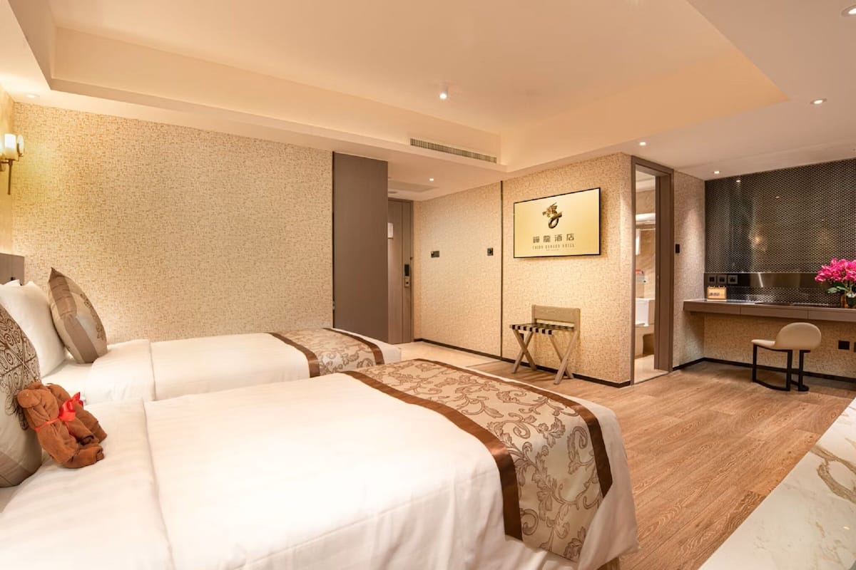 A hotel room with two beds, a small seating area, a kitchenette, and a bathroom.