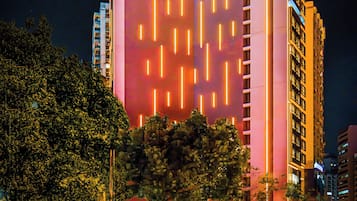 Un hotel alto con líneas verticales iluminadas en su fachada, un letrero que indica que es el Hotel China Dragon, y un estacionamiento con coches.