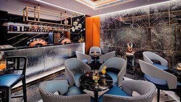 A bar area with a marble wall, a bar counter with various bottles, and seating with a round table.