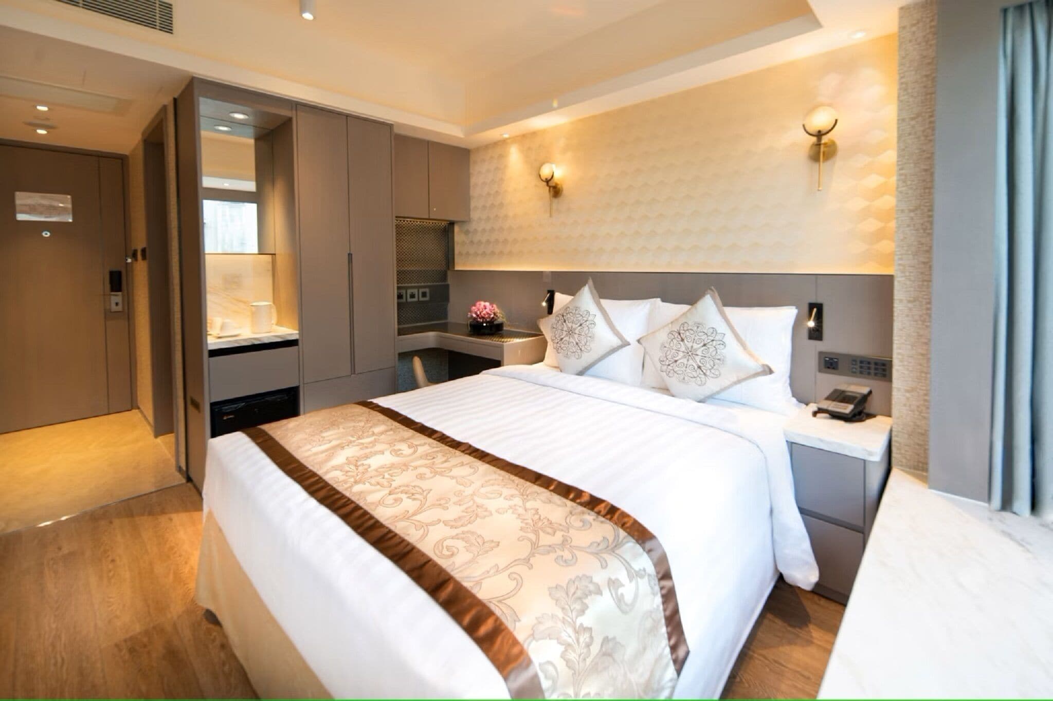 A hotel room with a large bed, a bedside table with a phone, a wall-mounted light, and a view of the room's interior.