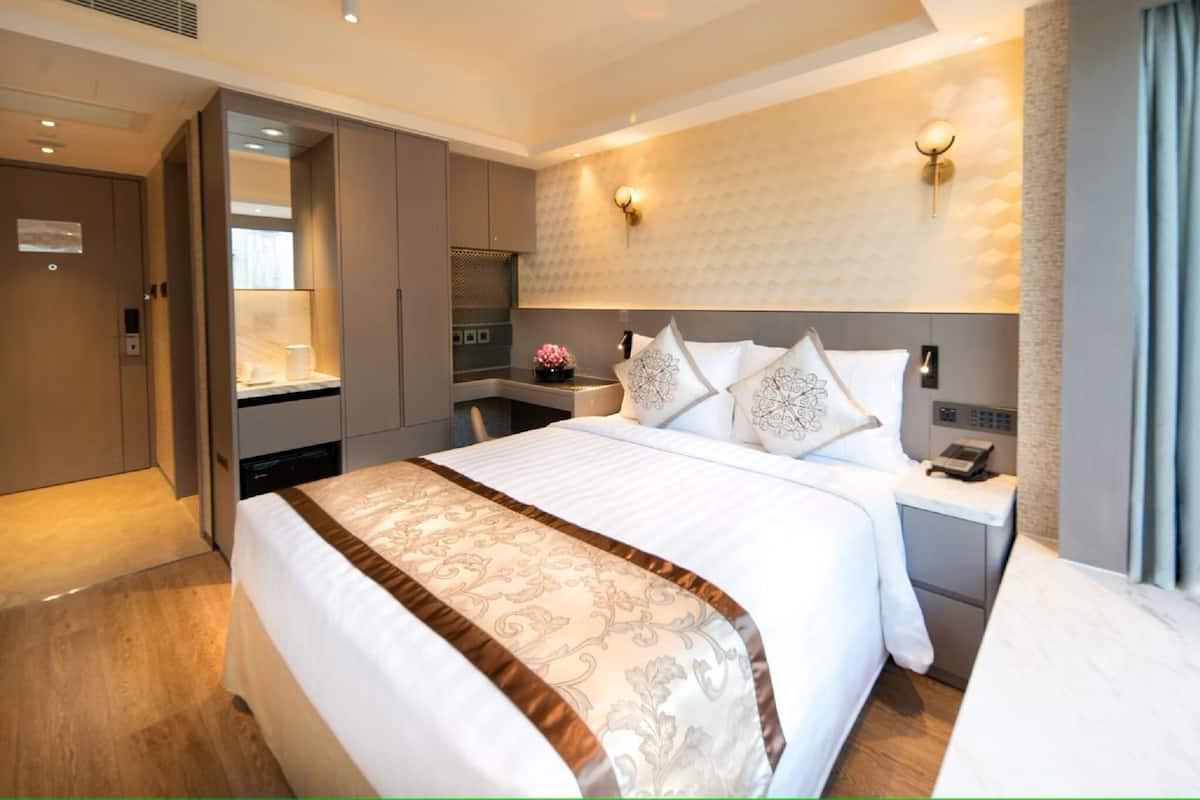 A hotel room with a large bed, a bedside table with a phone, a wall-mounted light, and a view of the room's interior.