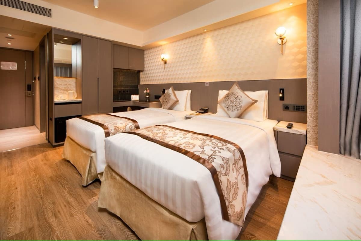 A hotel room with two beds, a minibar, a desk, and a shower area.