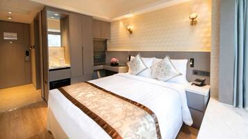 A hotel room with a large bed, a bedside table with a phone, a wall-mounted light, and a view of the room's interior.