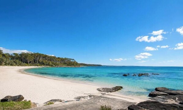 A beach with clear turquoise water, a sandy shore, and a forested area in the background.