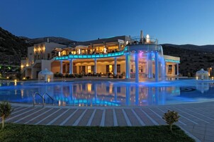 Un hotel con piscina, mobiliario exterior y montañas al fondo.