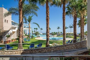 A pool area with palm trees, lounge chairs, and a building with a balcony. - Noverian Scenic Crete 5 Hilltop Villa Resort &spa (Hersonissos)