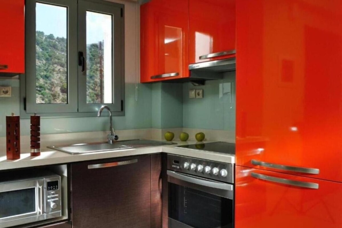 A kitchen with a sink, stove, oven, and a window with a view of a hillside.
