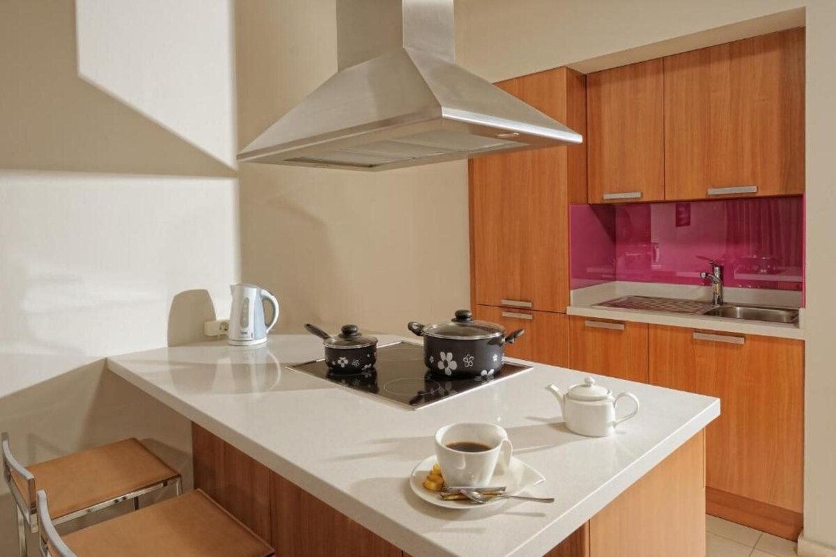 A compact kitchen with a white countertop, a kettle, a teapot, and a small stove.
