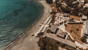 Luftaufnahme eines Küstenhotels mit Strand, Liegestühlen und Poolbereich.