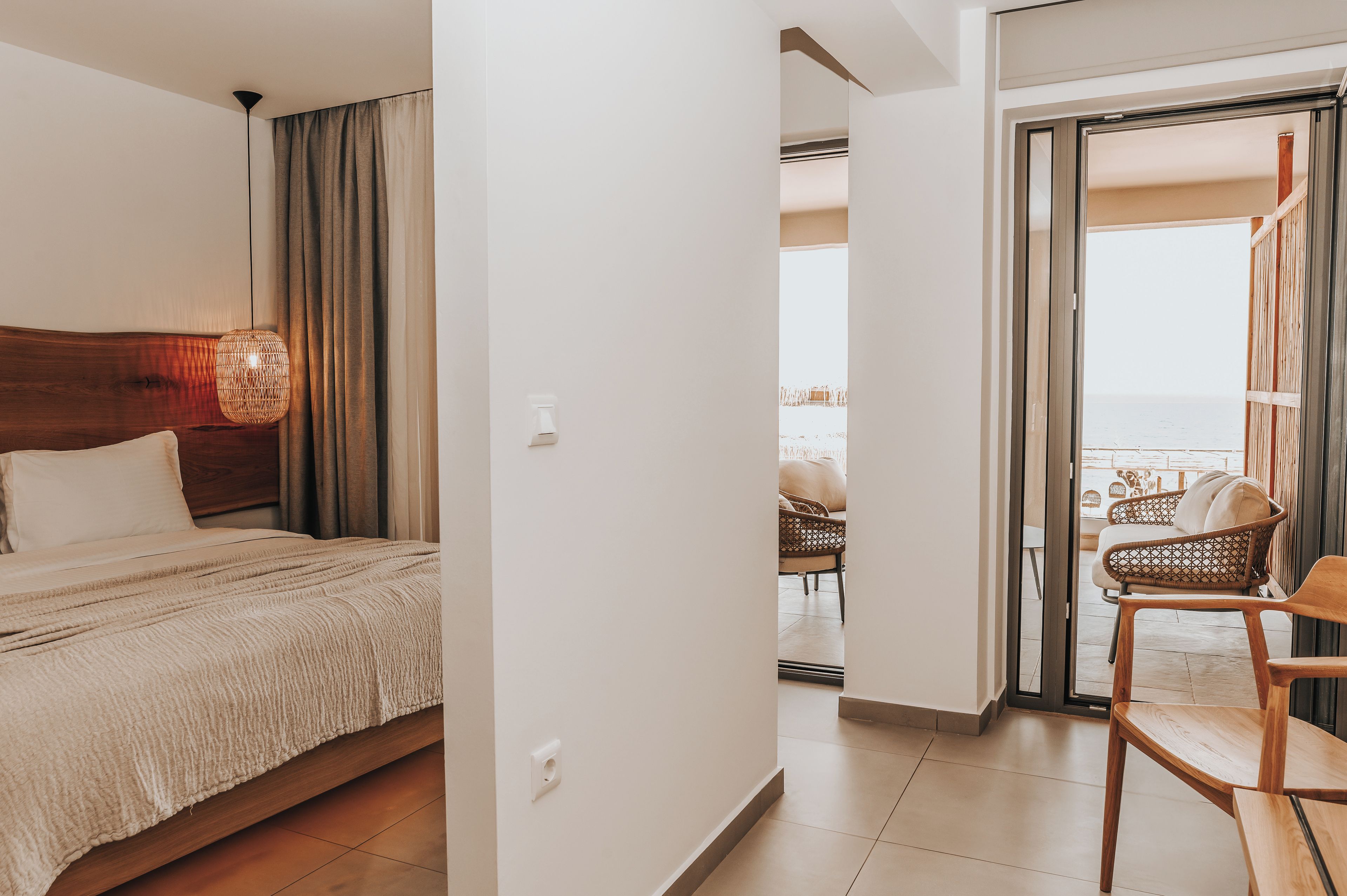 Une chambre d’hôtel avec un lit, un fauteuil en osier et une vue sur le balcon.