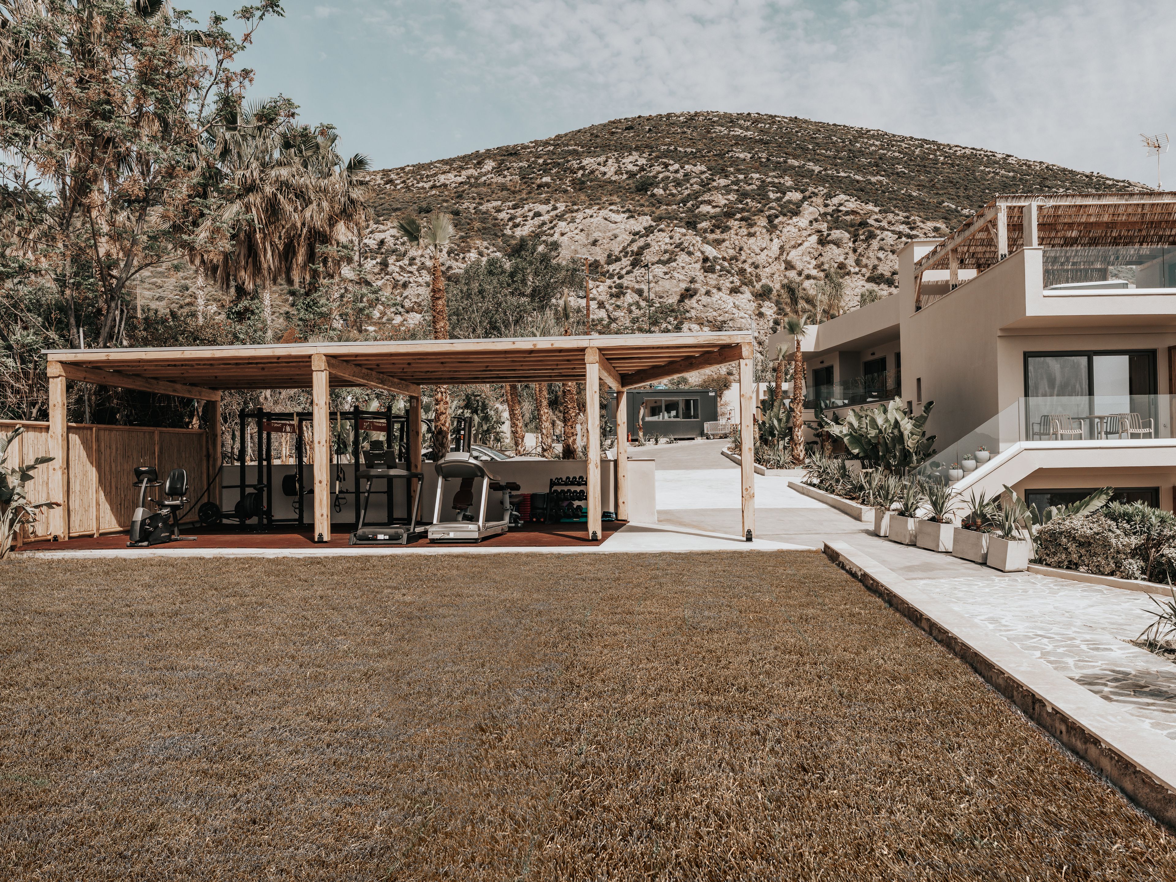 A modern outdoor gym area with exercise equipment, a covered seating area, and a view of a mountainous landscape.