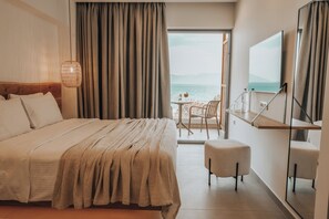 Habitación de hotel con cama, una mesita con sillas, televisión y vista al mar.