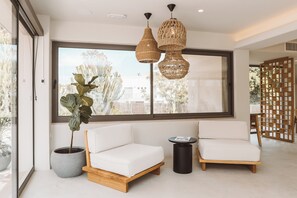 Een moderne woonkamer met een groot raam, twee witte banken, een potplant en twee geweven hanglampen.
