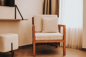 A wooden chair with a cushion, a small ottoman, and a flat-screen TV mounted on the wall. - Sagredo Boutique Hotel And Spa (Kos)