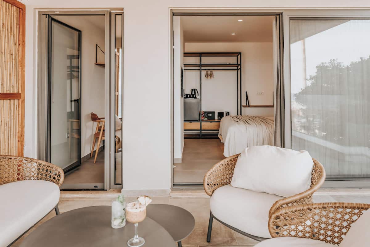 A modern hotel room with a balcony, a dining area, and a kitchenette.