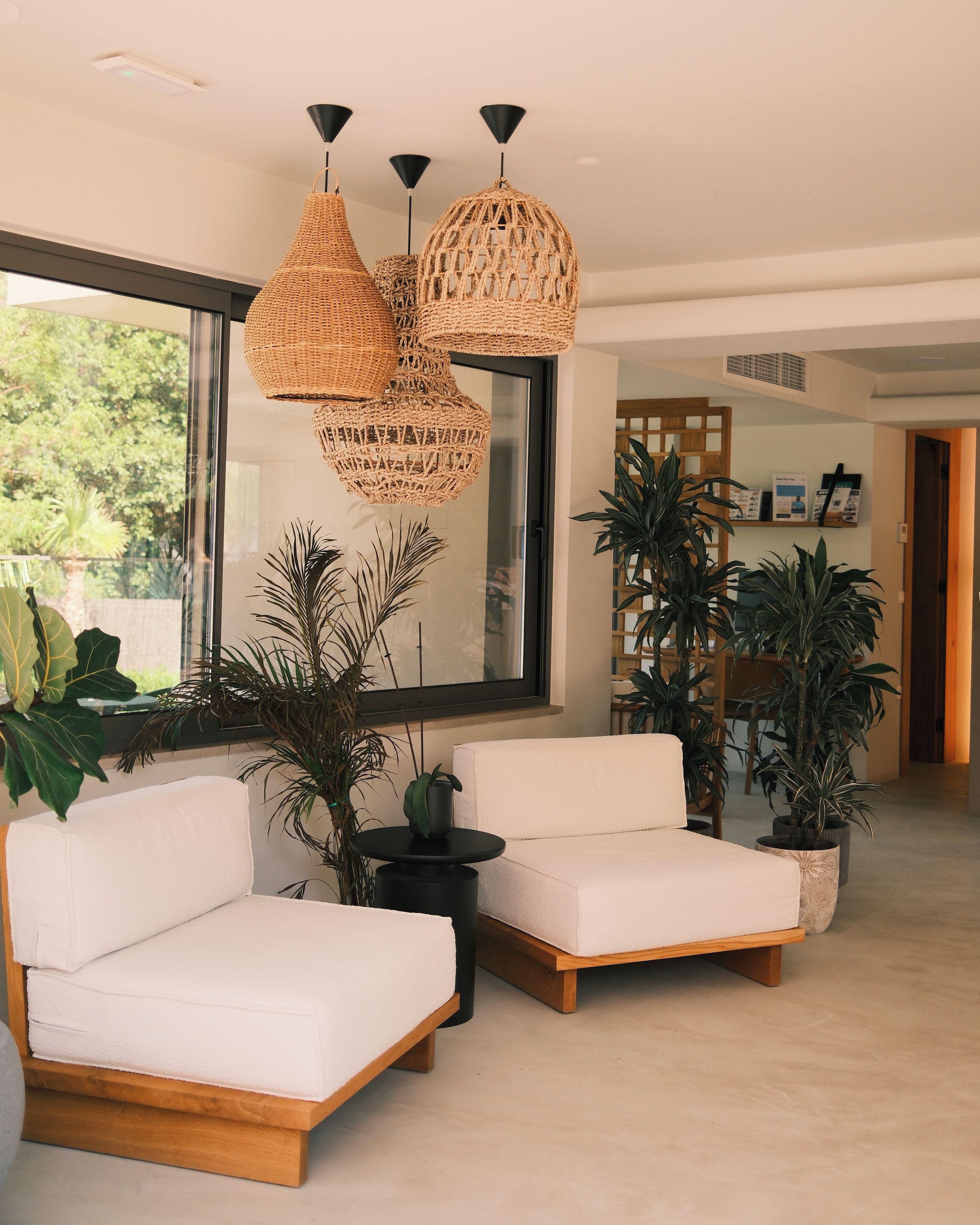 A modern living room with a large window, two white sofas, and multiple potted plants.