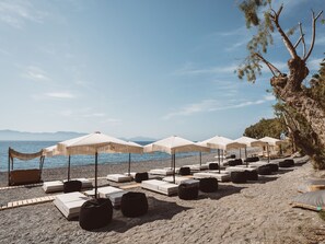 A beach with lounge chairs and umbrellas, a rocky shoreline, and a tree.