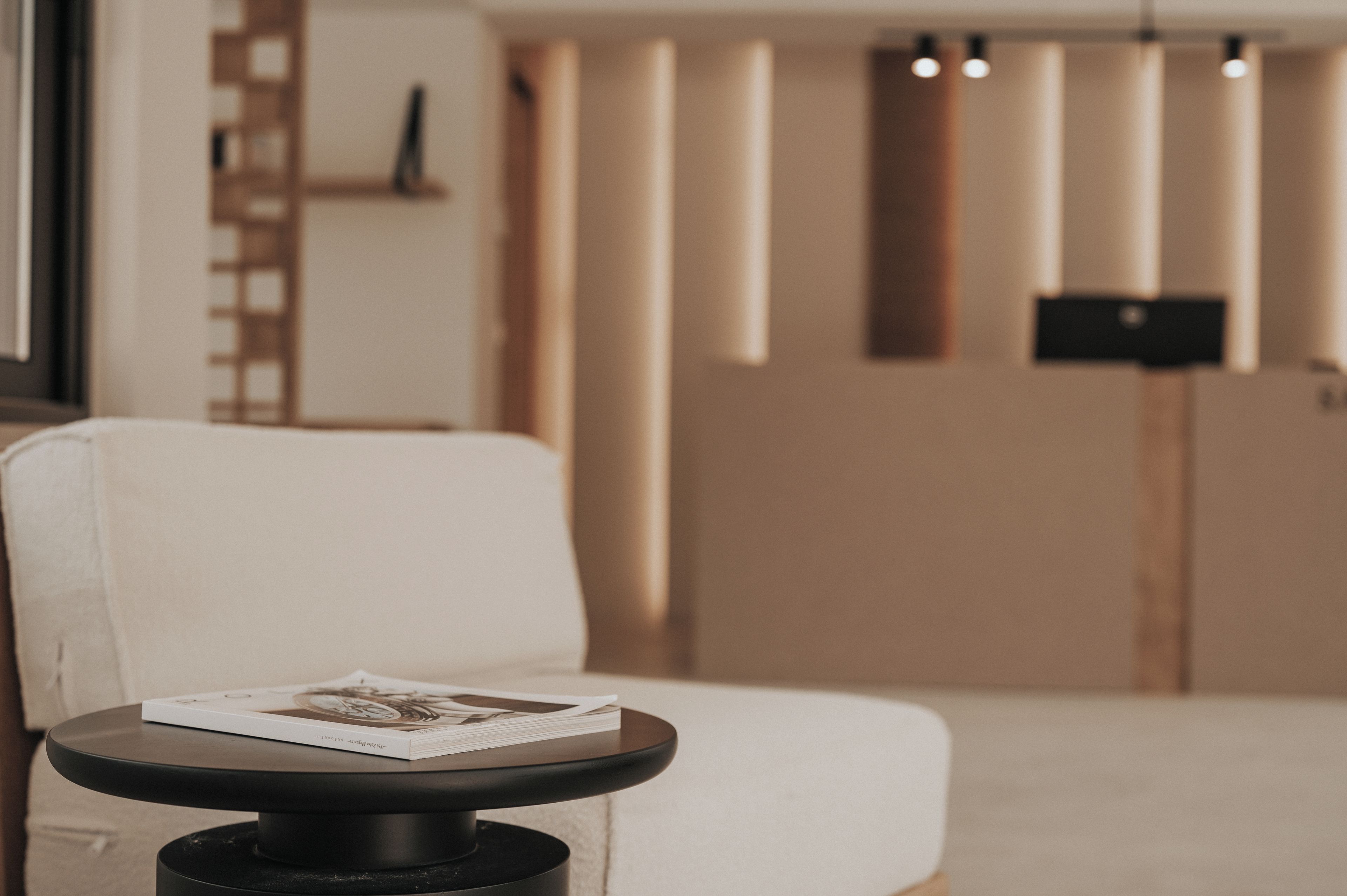 Ein modernes Wohnzimmer mit einem weißen Sofa, einem kleinen runden Tisch mit einer Zeitschrift und einem schwarzen Lautsprecher auf einem Ständer.