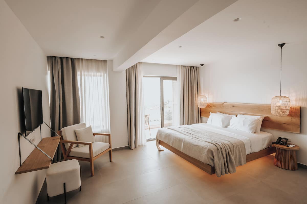 A modern hotel room with a bed, a desk, a chair, a TV, and a balcony.