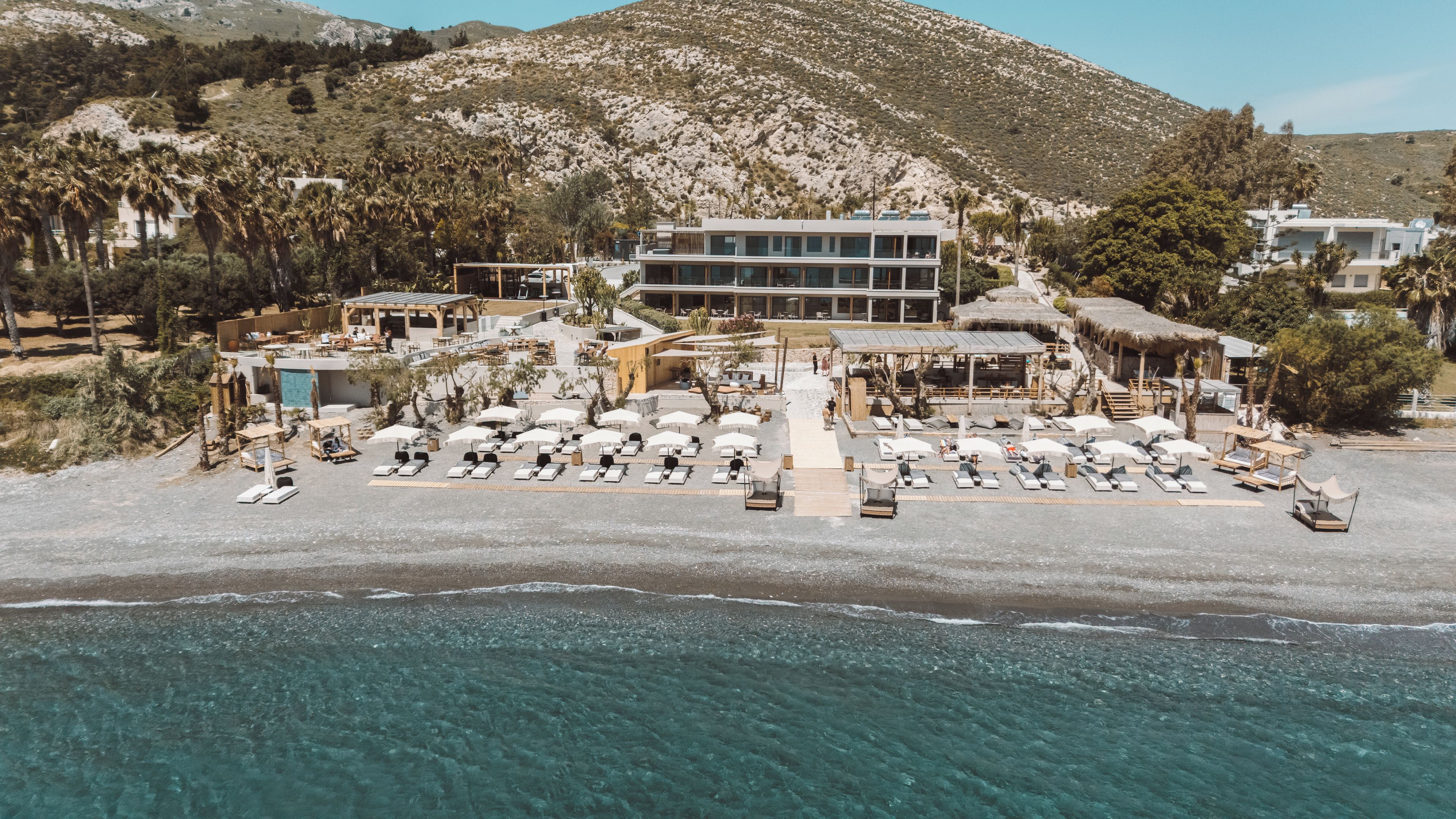 A beachside resort with multiple lounge areas, a pool, and a mountain backdrop.