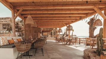 An outdoor patio with wooden furniture, woven chairs, and a thatched ceiling.