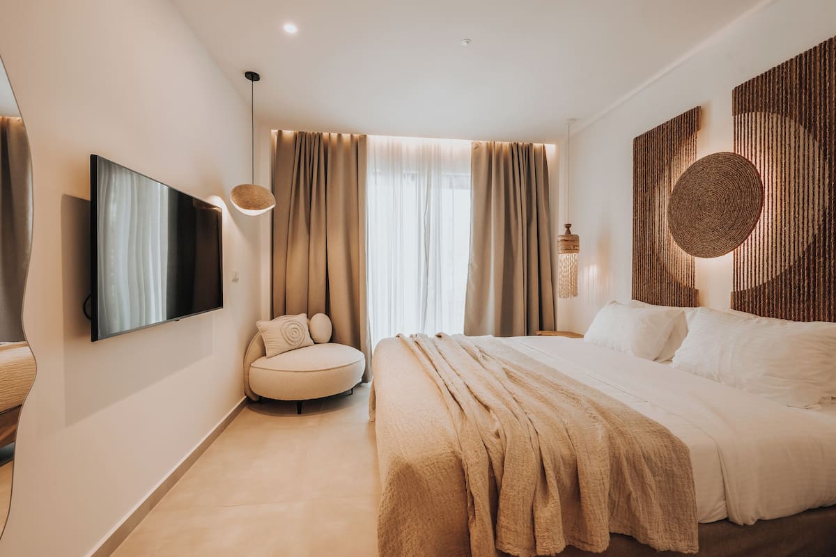 A modern bedroom with a bed, a round seating area, a television, and a large window with curtains.