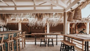A rustic outdoor dining area with wooden tables and chairs, straw ceiling, and stone walls. - Sagredo Boutique Hotel And Spa (Kos)
