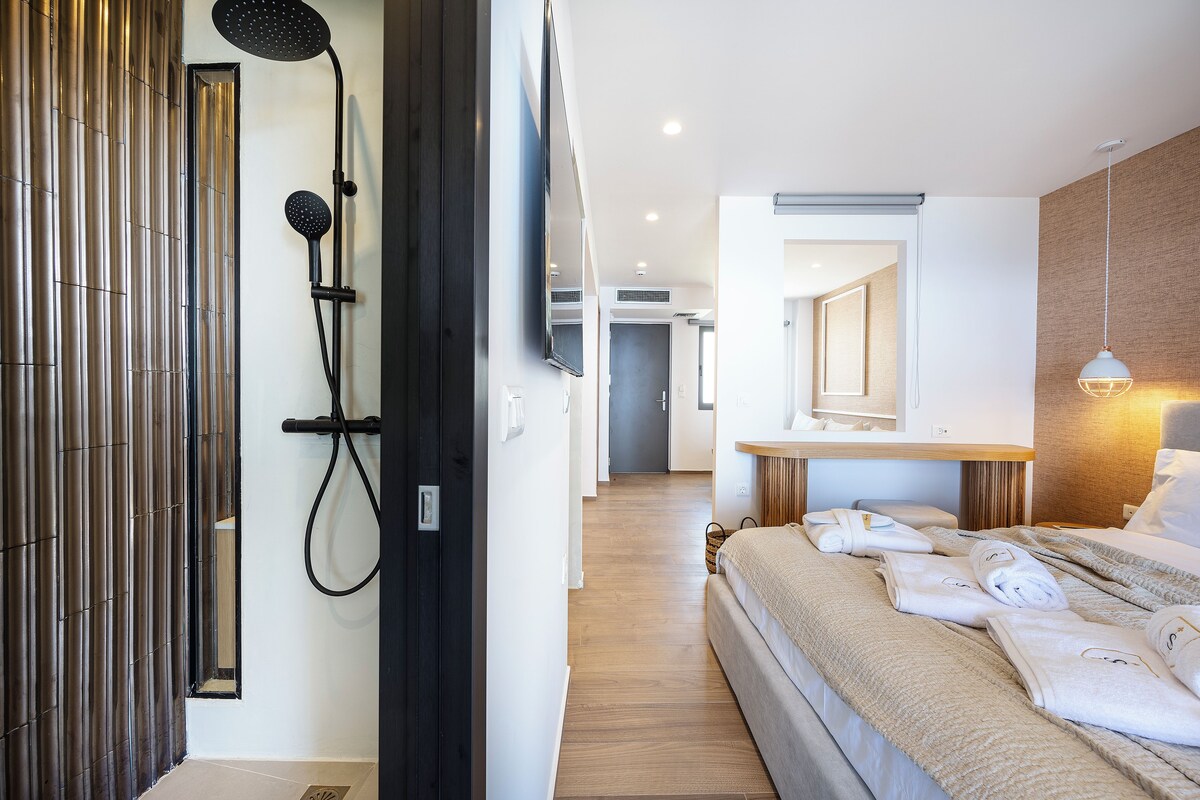 A modern hotel room with a shower, a bed with towels, a bedside table, and a mirror.