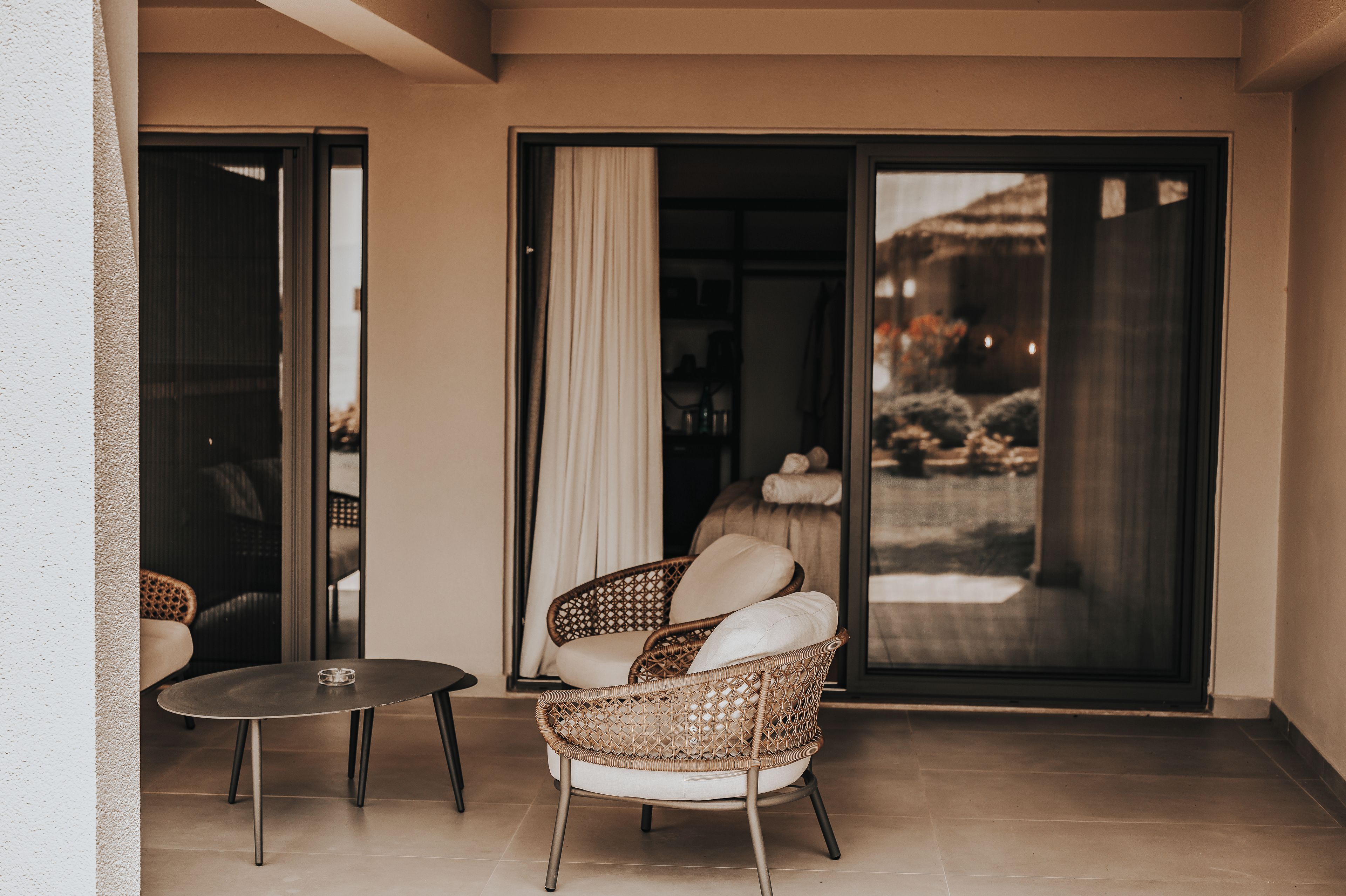 A balcony with a wicker chair, a small round table, and a sliding glass door leading to an outdoor area.