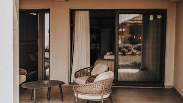 A balcony with a wicker chair, a small round table, and a sliding glass door leading to an outdoor area.