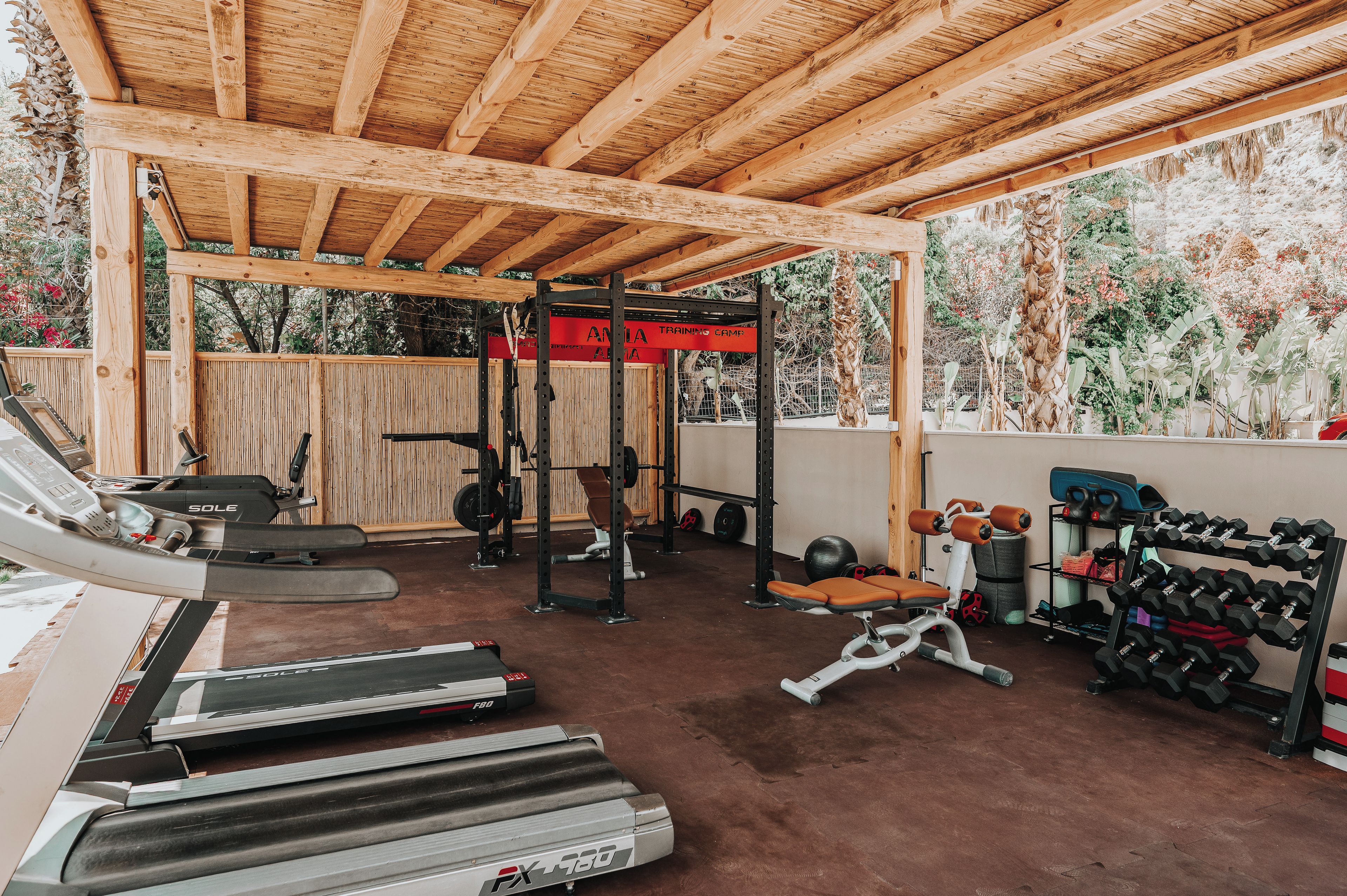 A covered gym area with treadmills, weight benches, and a squat rack.