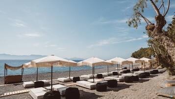 A beach with lounge chairs and umbrellas, a rocky shoreline, and a tree.